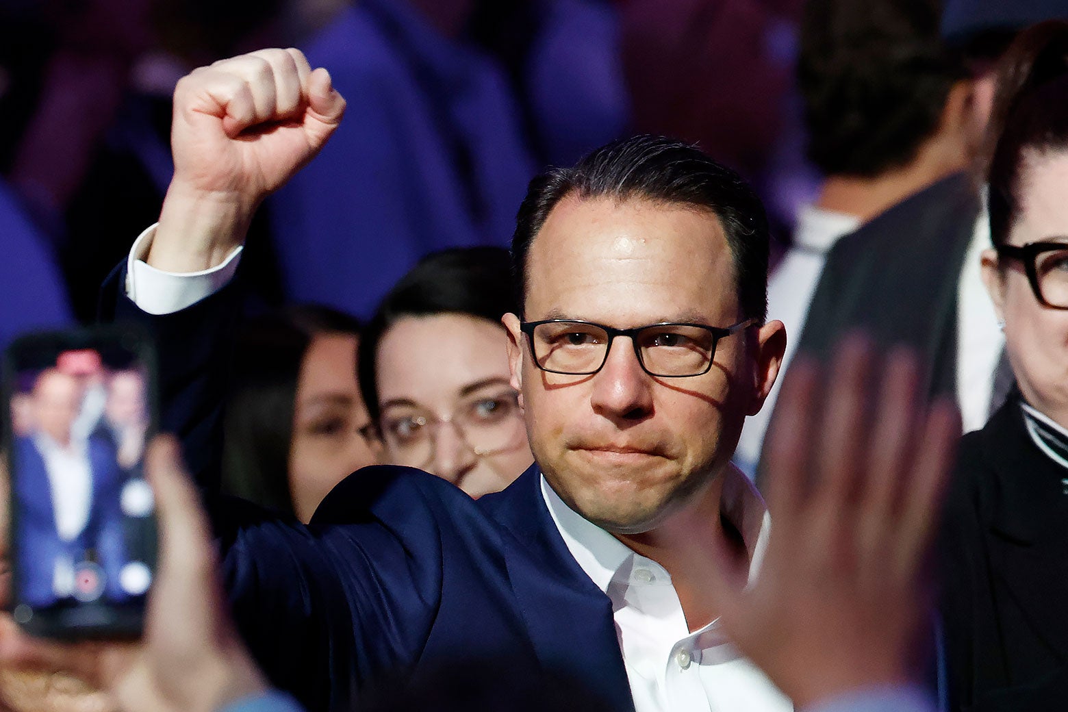 Gov. Josh Shapiro, his lips pursed in a serious _expression_, raises his right fist among a crowd of supporters.