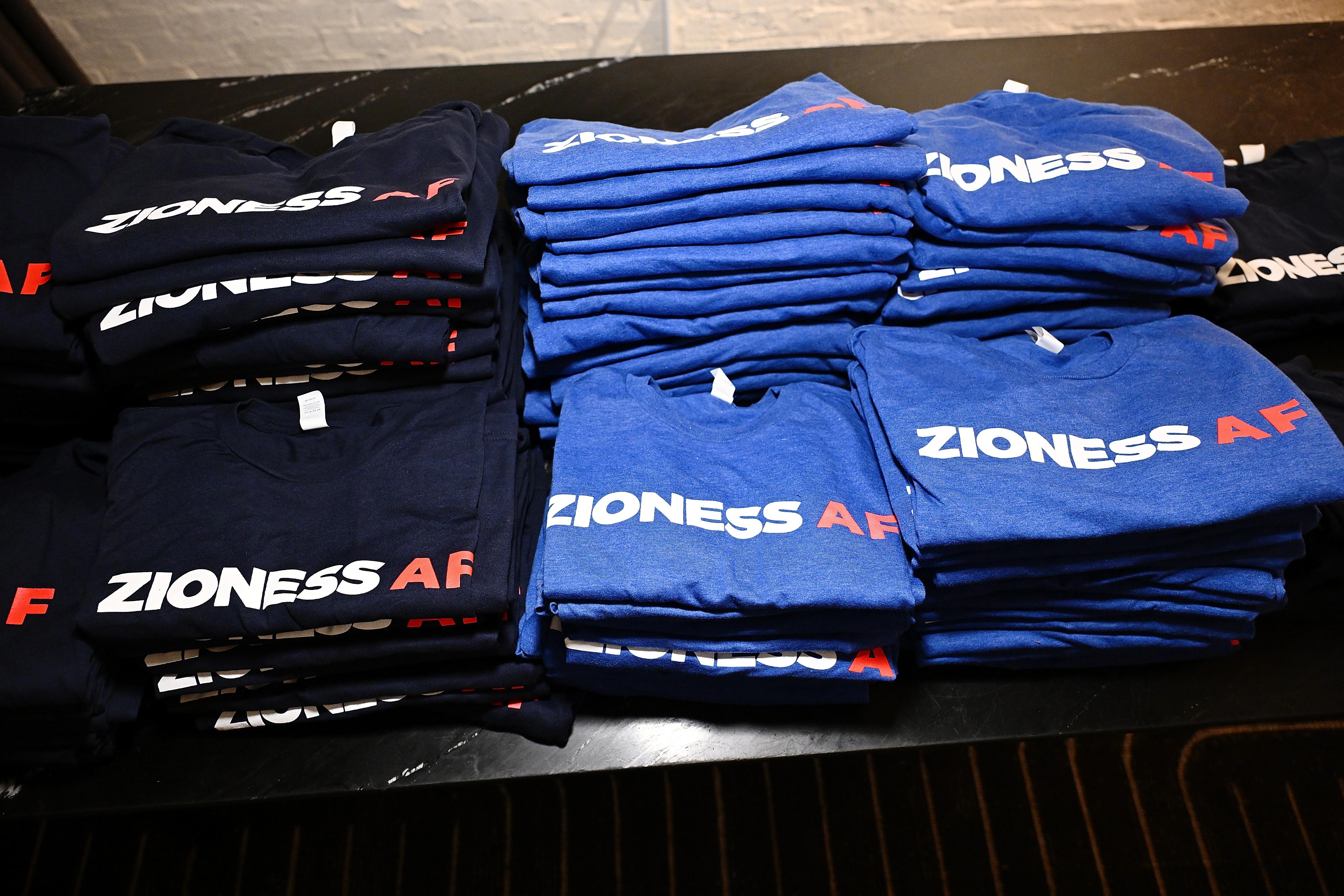 Folded black and blue T-shirts on a table that read "Zioness AF."