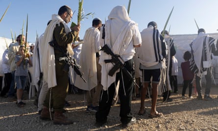 Backs of people standing in white shawls, some with guns, with blue sky above 