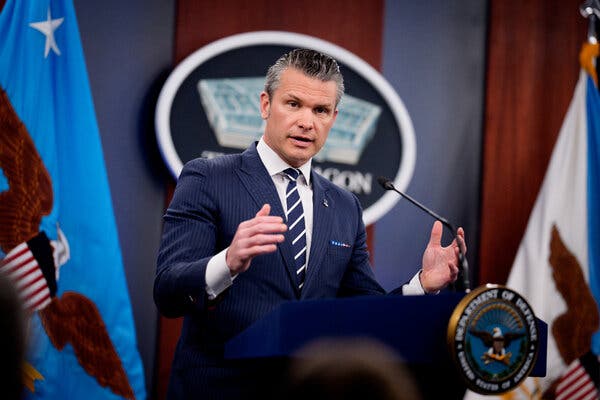 Hegseth is standing on the podium for a press conference, gesturing. 