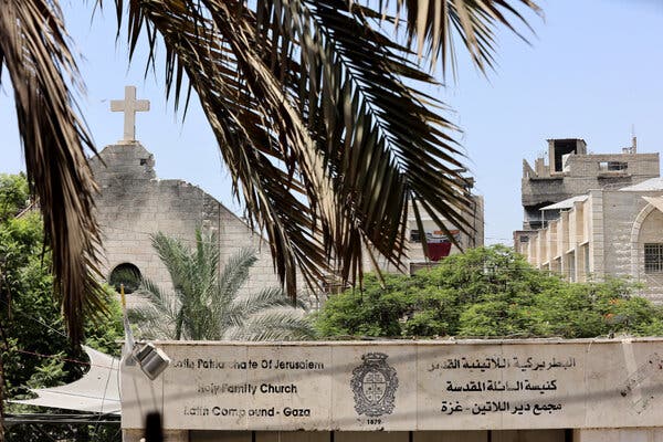A view through palm fronds of a church with some damage to its roof visible, and a sign in front in English and Arabic saying “Patriarchate of Jerusalem, Holy Family Church, Latin Compound — Gaza.”