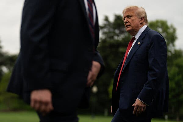 President Trump, in a red tie, walks past another person outdoors.