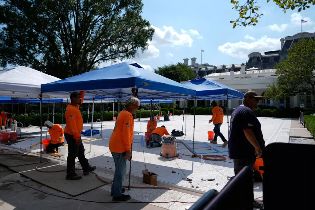 Workers, in orange shirts, apply tiles to what was the Rose Garden lawn in front of the White House.