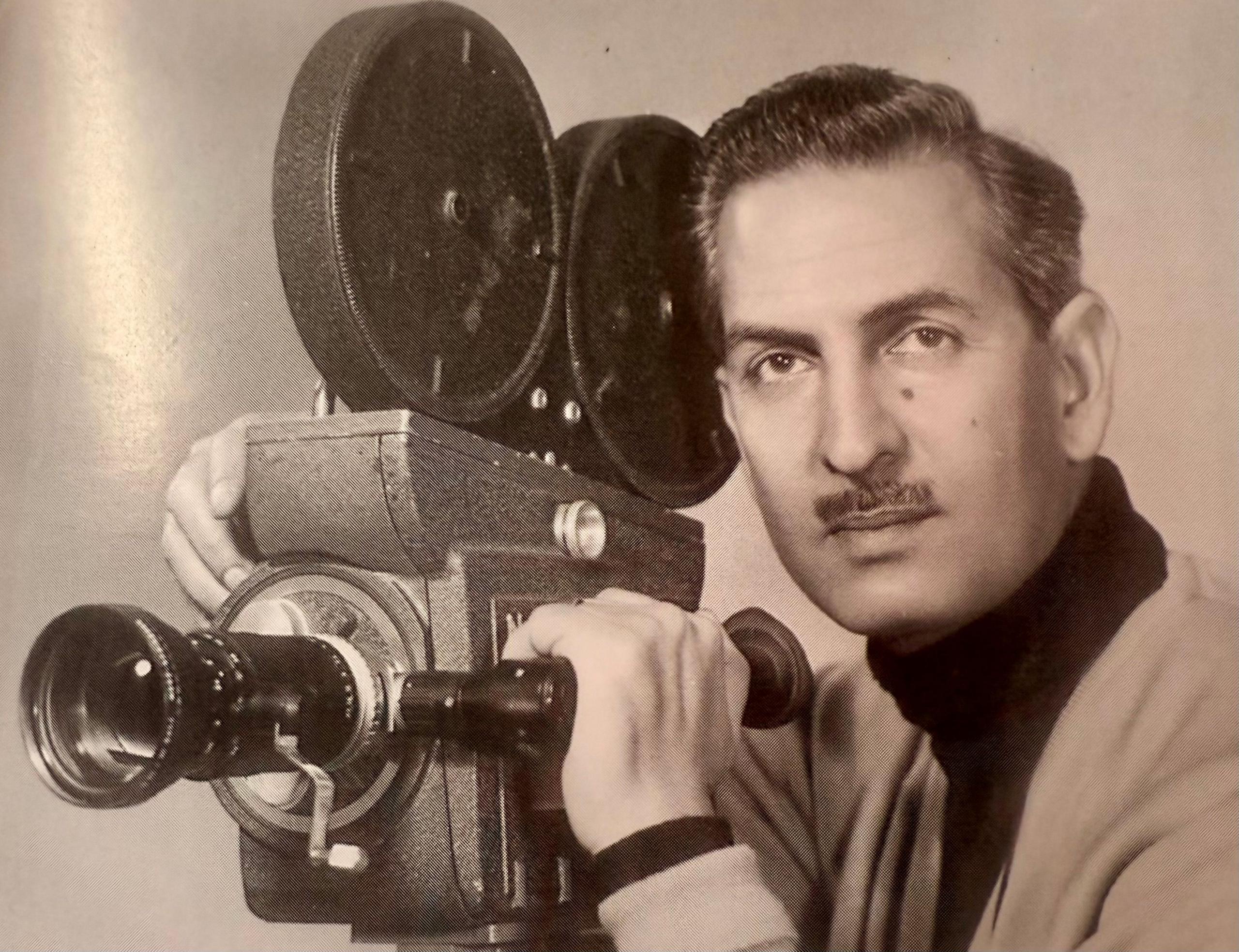 A younger Yavar pictured beside his camera from his days as cameraman and film-maker. He has a moustache and looks straight into the camera with a serious _expression_. 