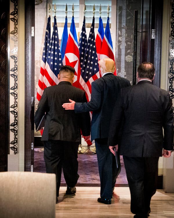Donald Trump and Kim Jong-un, seen from behind, walk into a room with U.S. and North Korean flags visible beyond.
