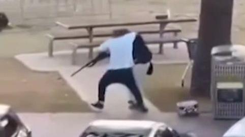 A still image of a man in a white t-shirt tackling a gun from a shooter 