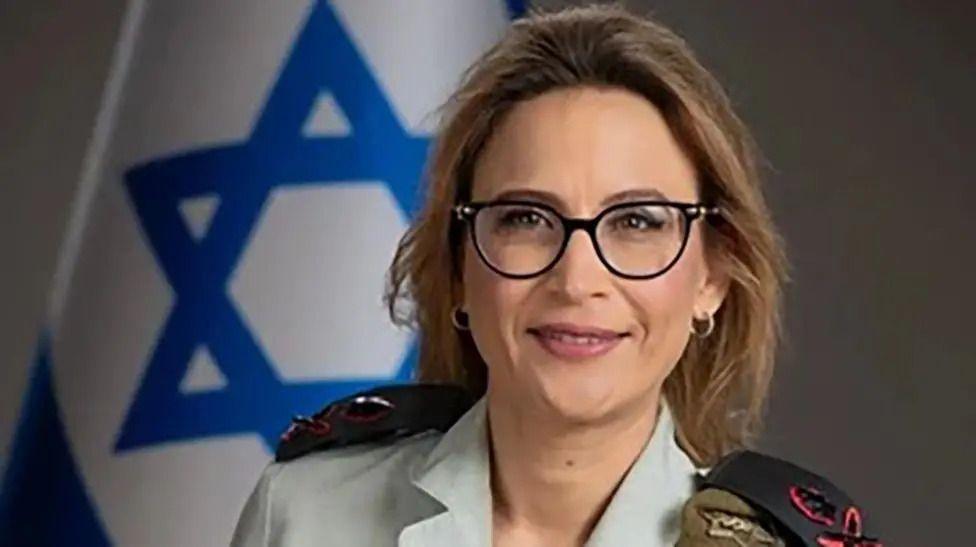 A handout image from the Israel Defense Forces shows a head shot of former Israeli Military Advocate General Yifat Tomer-Yerushalmi. She wears glasses and is smiling at the camera, with an Israeli flag visible in the background. 