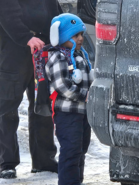 child wearing plaid shirt and blue stands in front of car