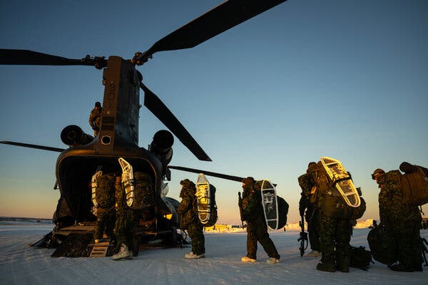 A dark helicopter with an open doorway on a snowy landscape. Several people are approaching to board.