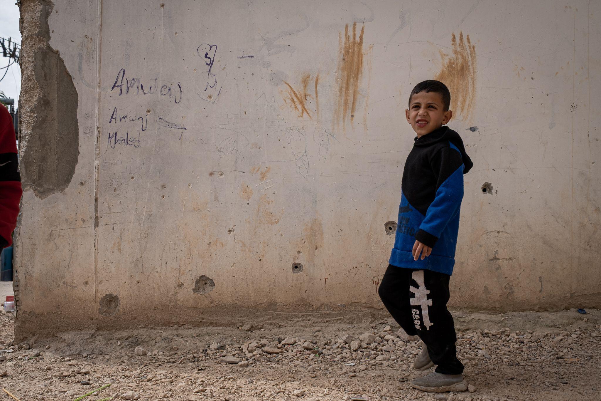 Bullet holes rake the wall in al-Far'a refugee camp, in the occupied West Bank, at the place CCTV shows Jad being shot from close range by an Israeli soldier. A young boy stands in the foreground of the image.