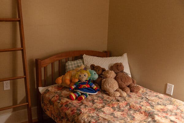 A number of stuffed toys sit on top of the bedspread on a made-up bed. A ladder rests against the wall next to the bed.