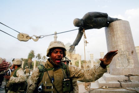 A US marine shouts and gestures with a toppled statue of Saddam Hussein behind him