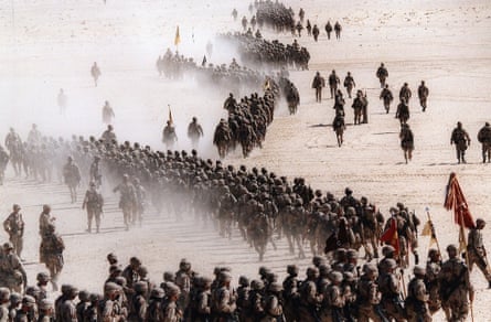 Troops march in columns across sandy ground
