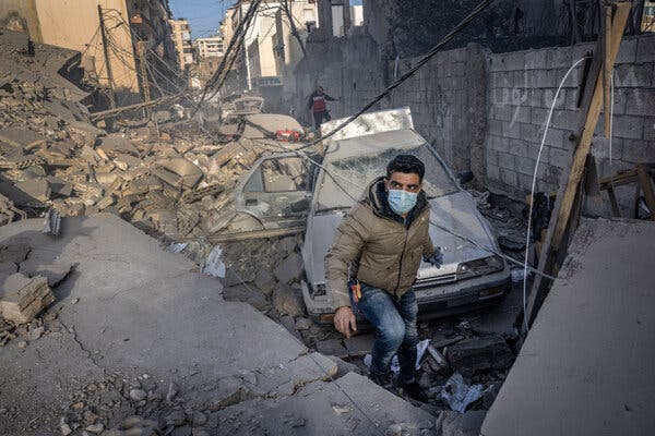 A man wearing a face mask making his way through rubble after an airstrike, with battered cars amid the wreckage.