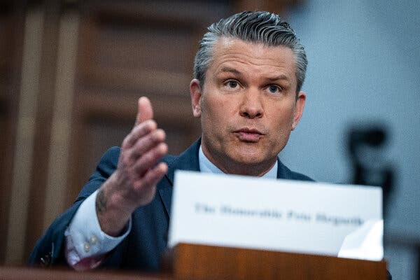 Defense Secretary Pete Hegseth, wearing a dark suit, motions with his right hand.