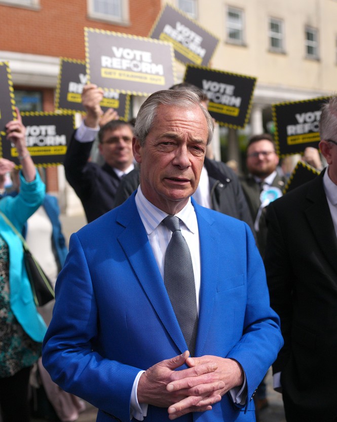 photo of white-haired man in bright blue suit and gray tie standing in front of crowd holding VOTE REFORM campaign signs