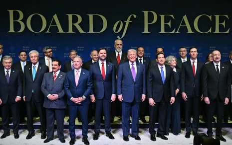 A group of men in suits smile in front of a backdrop that reads 'Board of Peace'