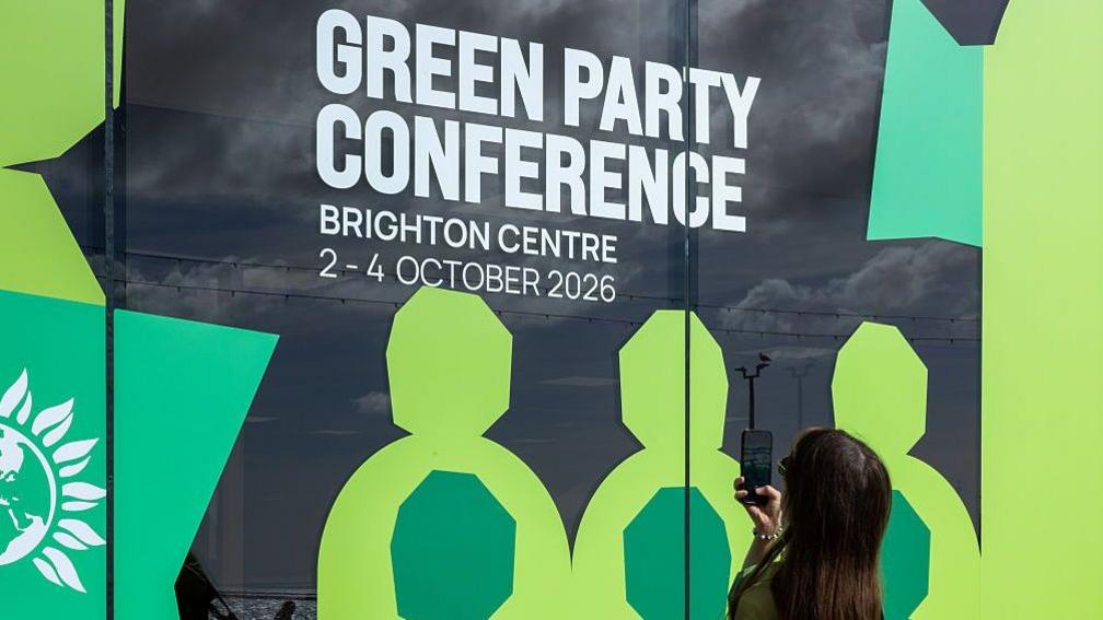 A woman takes a photo of sign advertising the Green Party conference. 